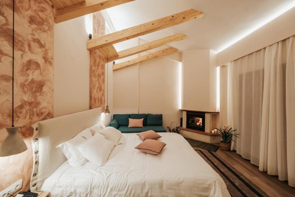 Um quarto com cama, sofá verde, lareira e janela com cortinas.