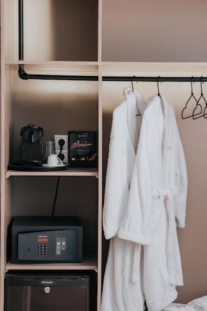 Habitación de hotel con minibar, cafetera y bata colgada en un perchero.