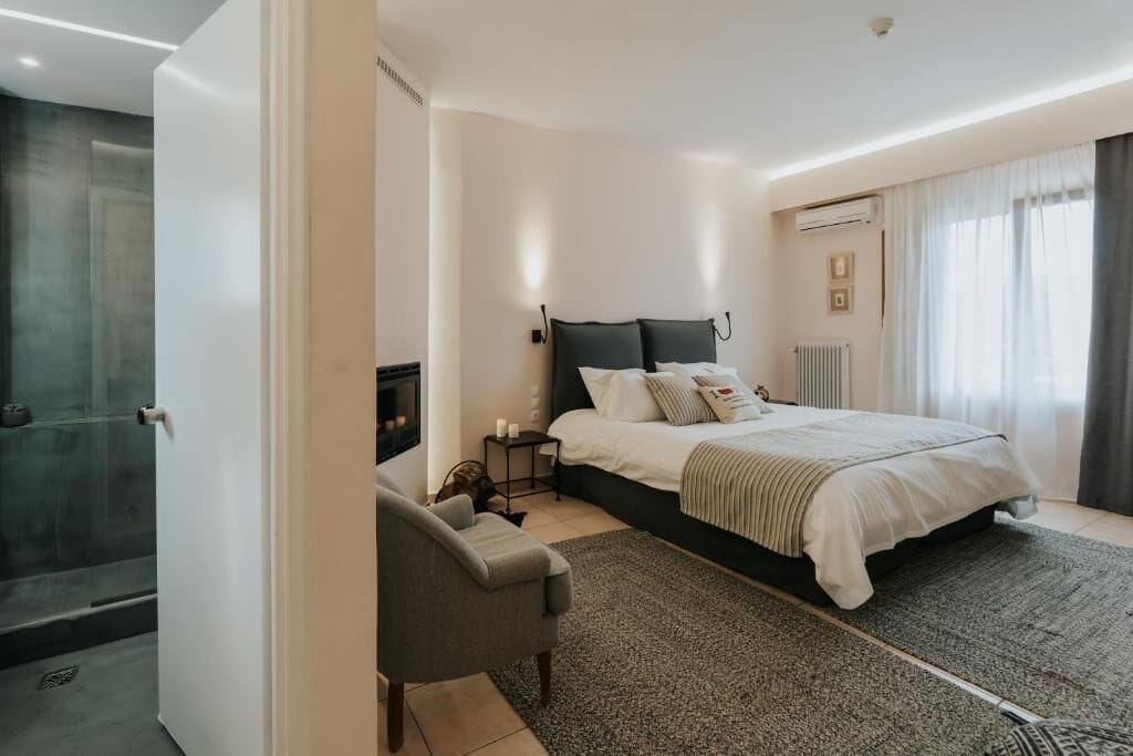 A bedroom with a bed, bedside table, chair, and a view of a bathroom.