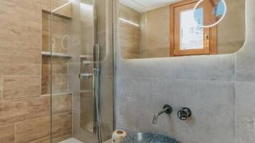 Un baño con ducha de vidrio, lavabo de madera y espejo sobre el lavabo.