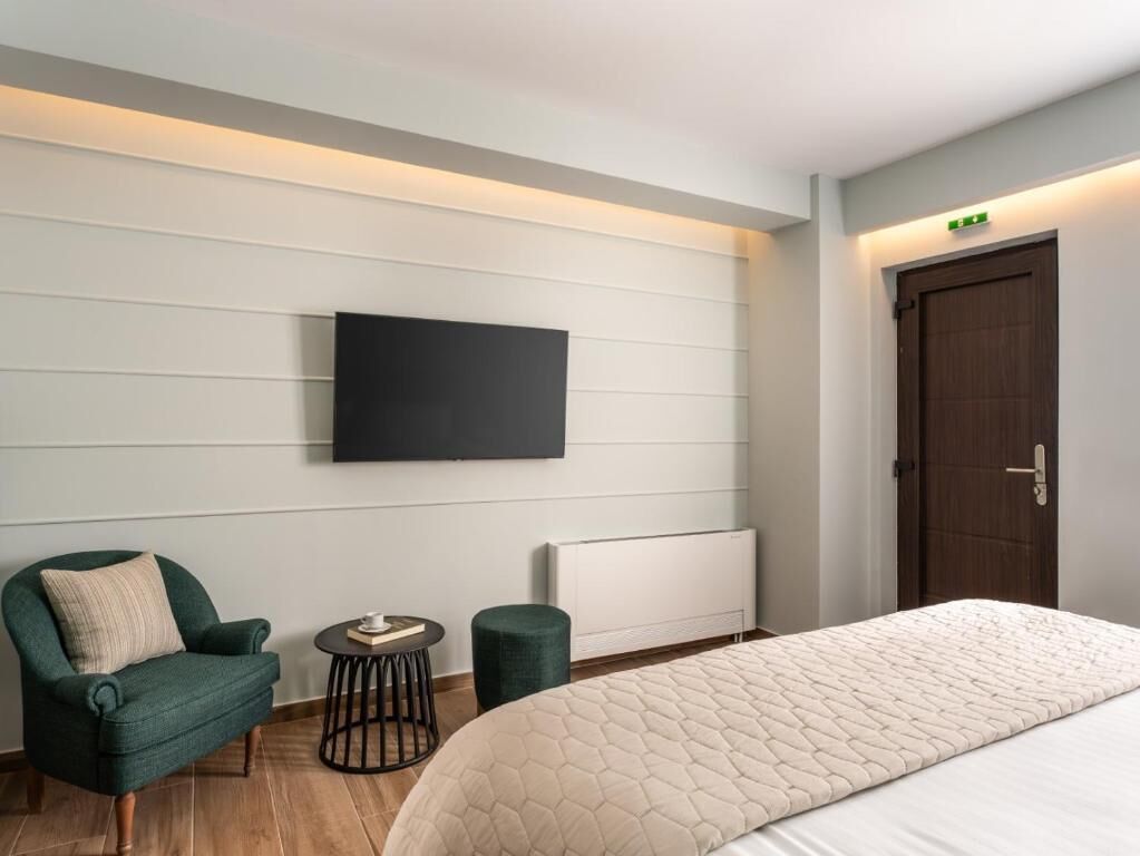 Habitación de hotel con una cama, televisión montada en la pared, una silla, una mesita redonda y un radiador.