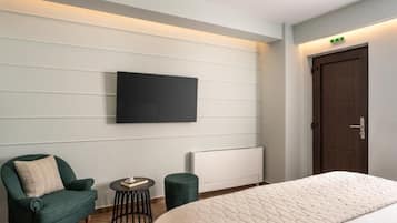 Habitación de hotel con una cama, televisión montada en la pared, una silla, una mesita redonda y un radiador.
