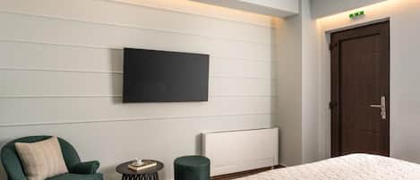 Habitación de hotel con una cama, televisión montada en la pared, una silla, una mesita redonda y un radiador.