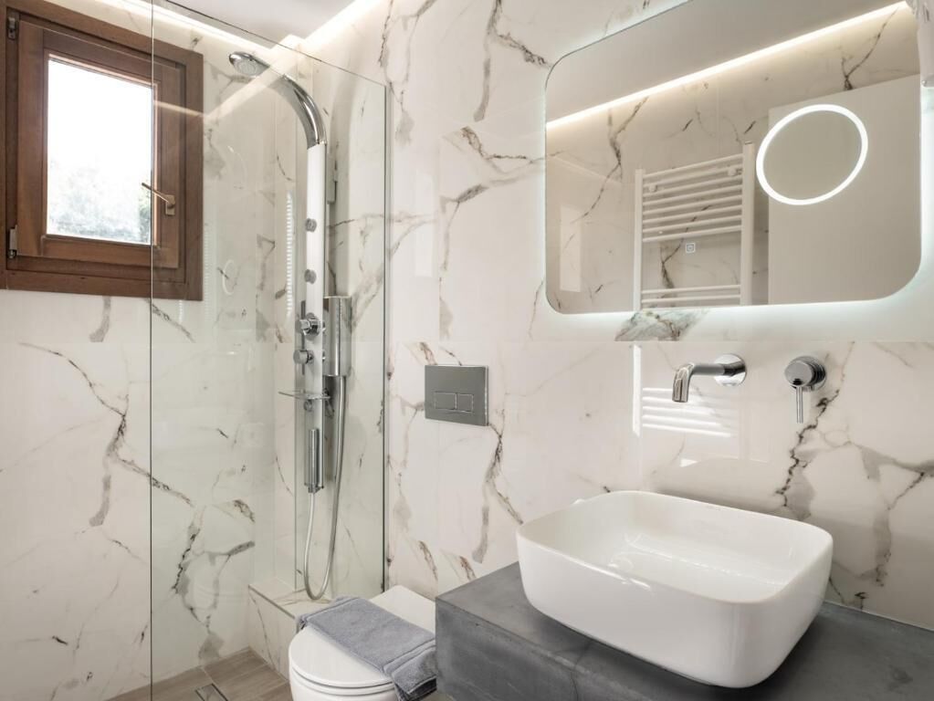 A modern bathroom with a glass-enclosed shower, a white sink, and a marble-patterned wall.