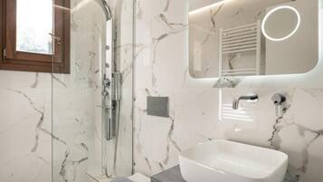 A modern bathroom with a glass-enclosed shower, a white sink, and a marble-patterned wall.