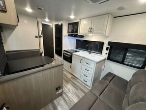 A compact RV interior with a kitchenette, a dining area, and a seating space. - RV with great Mountain View with picnic area, ponds, trails and fruits trees (Hamden)