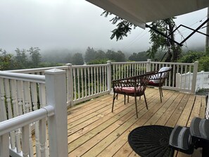 A wooden deck with white railings, two wicker chairs with cushions, and a black rug. - RV with great Mountain View with picnic area, ponds, trails and fruits trees (Hamden)