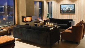 A modern living room with a large sofa, a television, and a fireplace. - High ceilings with a view of the ski slopes (Hovden)