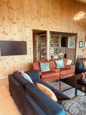 A modern living room with a wooden wall, a sectional sofa, a coffee table, and a wine rack. - High ceilings with a view of the ski slopes (Hovden)