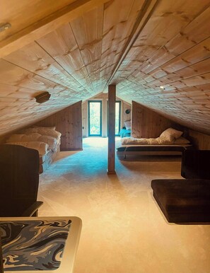Ein Schlafzimmer im Dachgeschoss mit schrägen Wänden, zwei Betten, einem großen Fenster und Blick ins Freie.