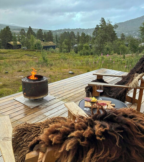A wooden deck with a fire pit, outdoor seating, and a view of a hilly landscape.