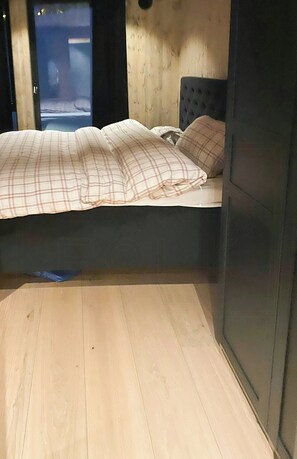 Ein Zimmer mit einem Bett, Holzboden und Blick durch eine offene Tür.