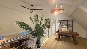 Een moderne woonruimte met een plafondventilator, een eethoek met een tafel en stoelen, een trap en een grote potplant.