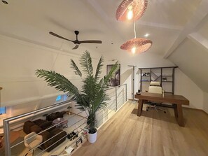 Een moderne woonruimte met een plafondventilator, een eethoek met een tafel en stoelen, een trap en een grote potplant.