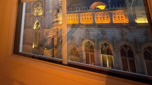 Une fenêtre donnant sur un bâtiment historique, caractérisé par ses fenêtres en arc et son clocher.