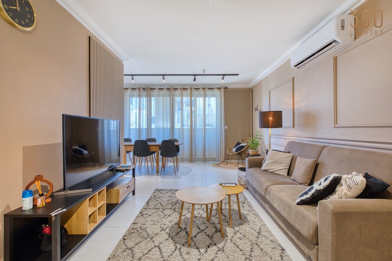 A modern living room with a flat-screen TV, a sofa, a coffee table, and a dining area with chairs.