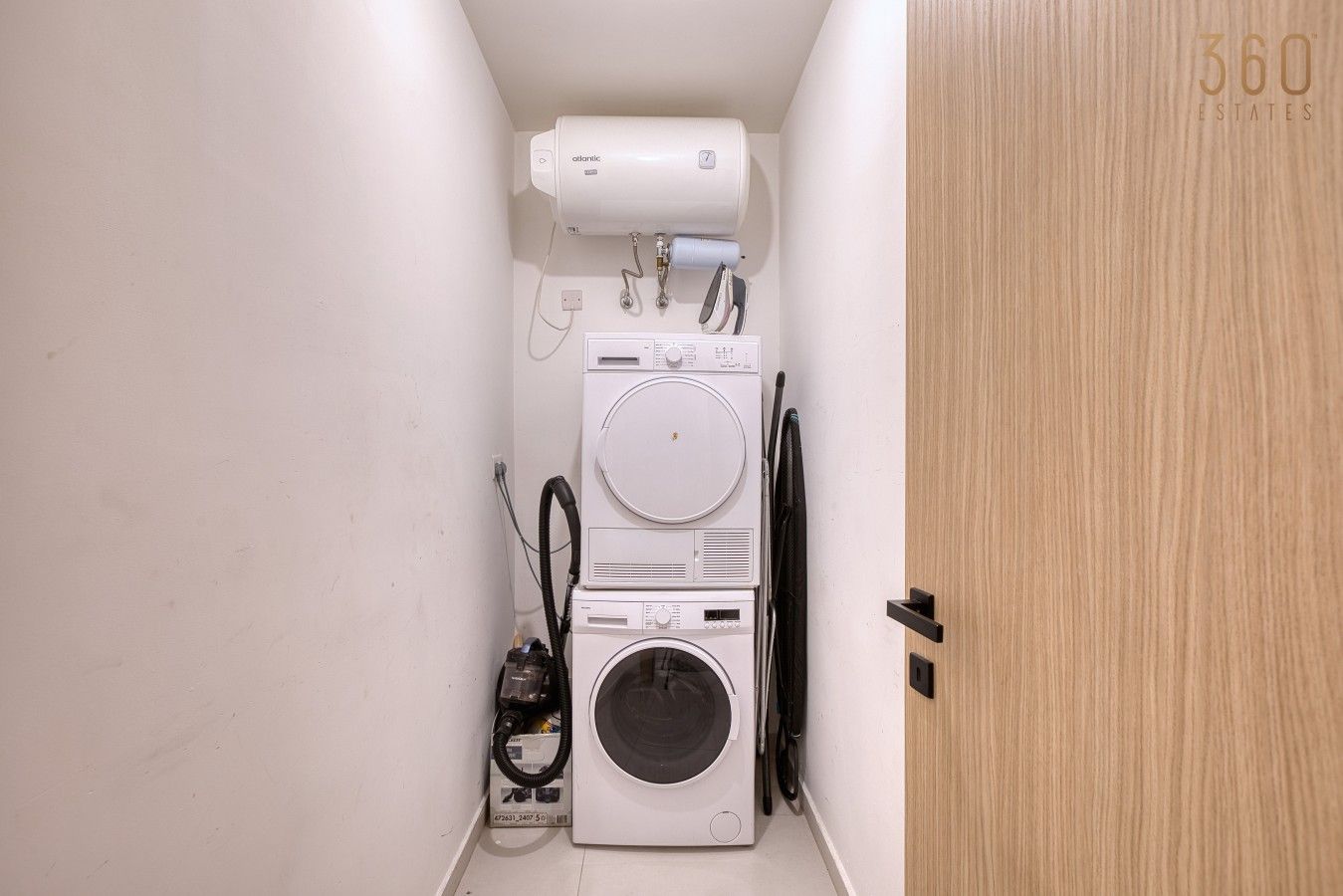 Un lavadero pequeño con lavadora y secadora apiladas, un calentador de agua y una puerta con la inscripción '360 ESTATES'.