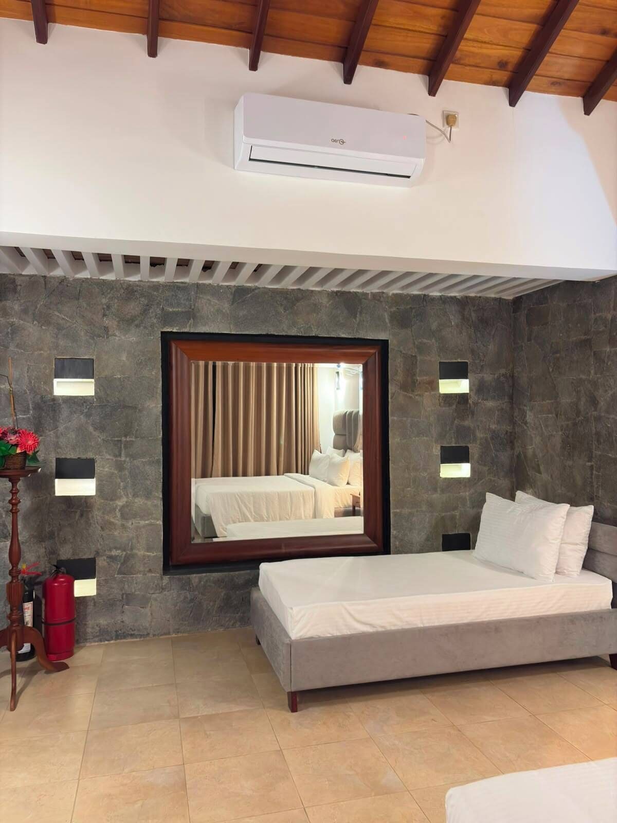 A bedroom with a bed, a window with curtains, an air conditioning unit, and stone walls.