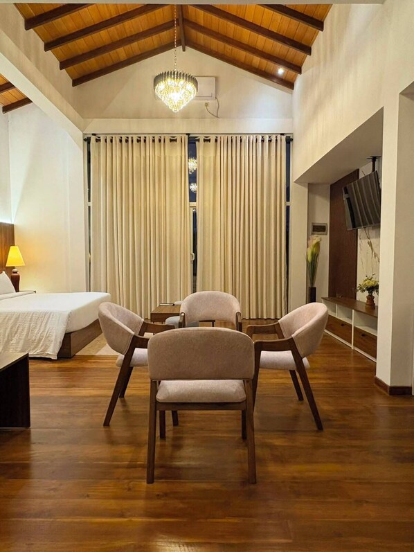 Una habitación con techo de madera, un candelabro, una cama, un escritorio, una silla y un televisor en la pared.