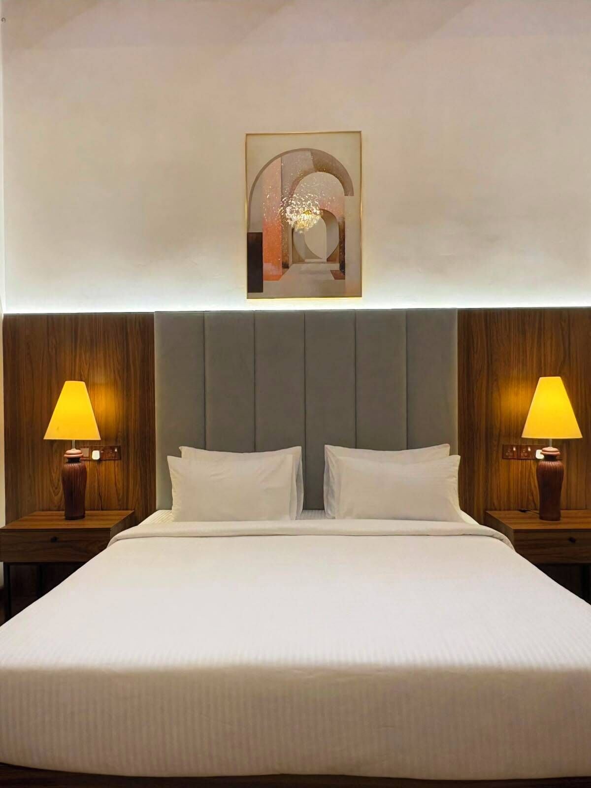 Una camera d'hotel con un letto grande, due lampade ai comodini, una testiera in legno e un quadro appeso al muro.