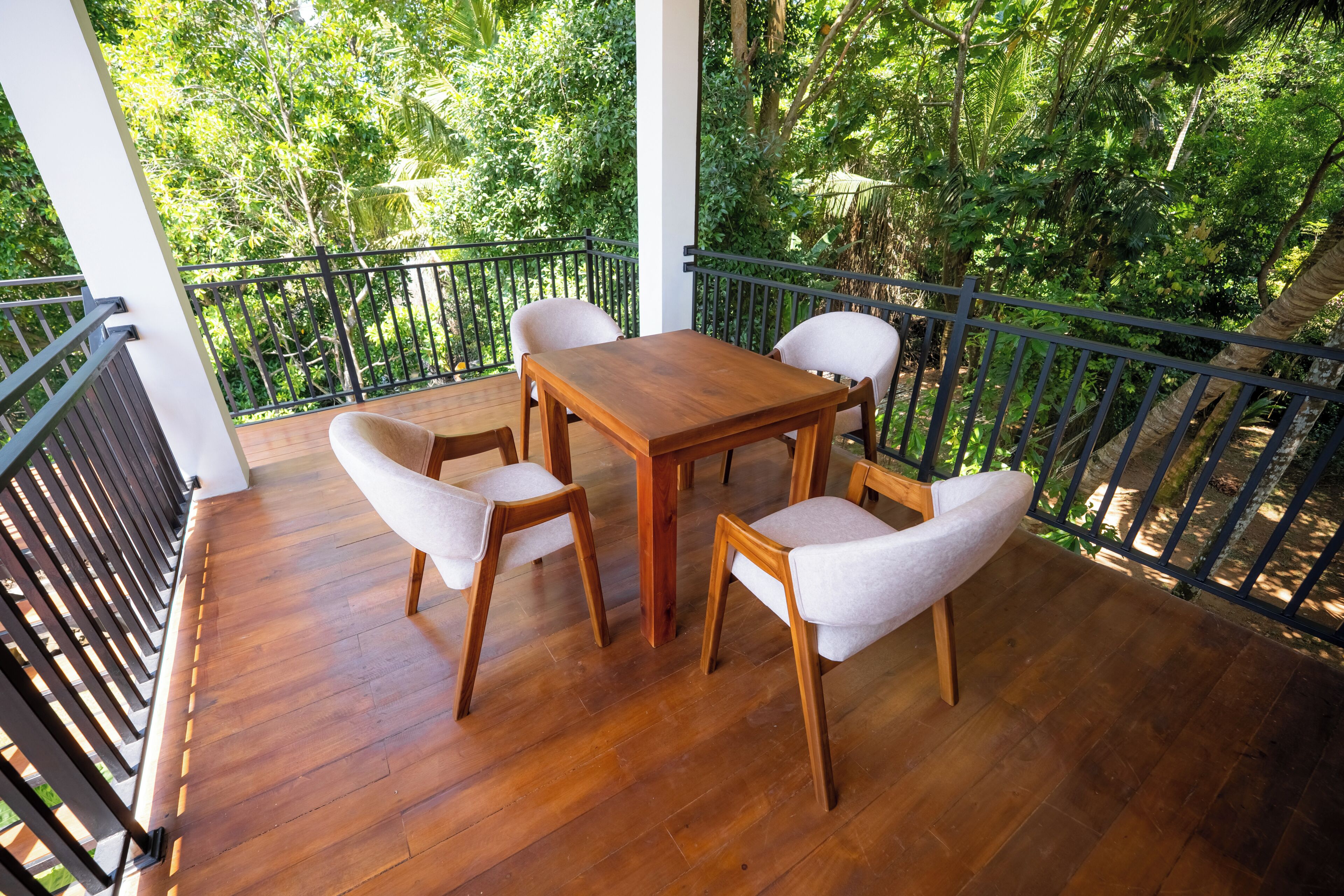 Eine Holzterrasse mit Tisch und Stühlen, umgeben von einem Metallgeländer, mit Blick auf einen üppigen Grünstreifen.