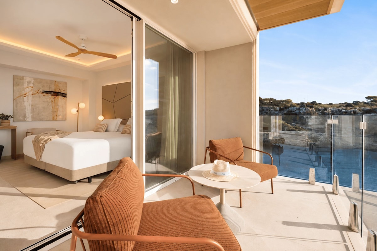 Quarto moderno com cama grande, escrivaninha e varanda com vista para o mar.