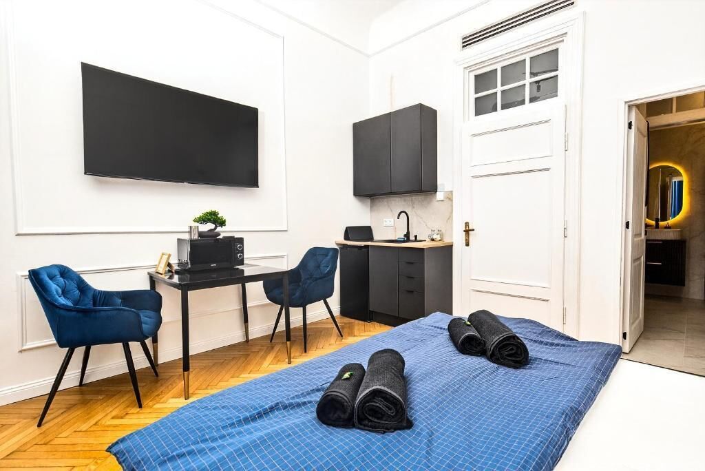 Une pièce de taille modeste comprenant un lit, un bureau avec une chaise, un téléviseur et un petit coin cuisine.