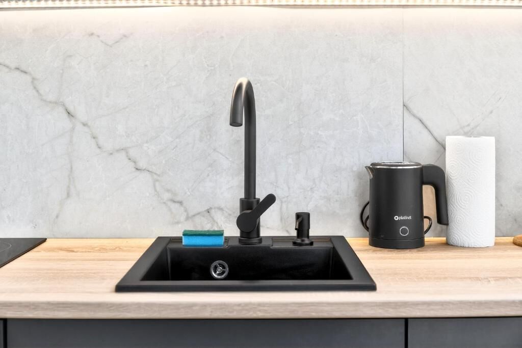 Een moderne keuken met een zwarte kraan, een koffiezetapparaat en een rol keukenpapier op het aanrecht.
