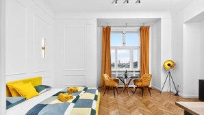 Hotellihuone, jossa on sänky, ruokapöytä, kaksi tuolia, lattiavalaisin ja ikkuna, jossa on verhot.