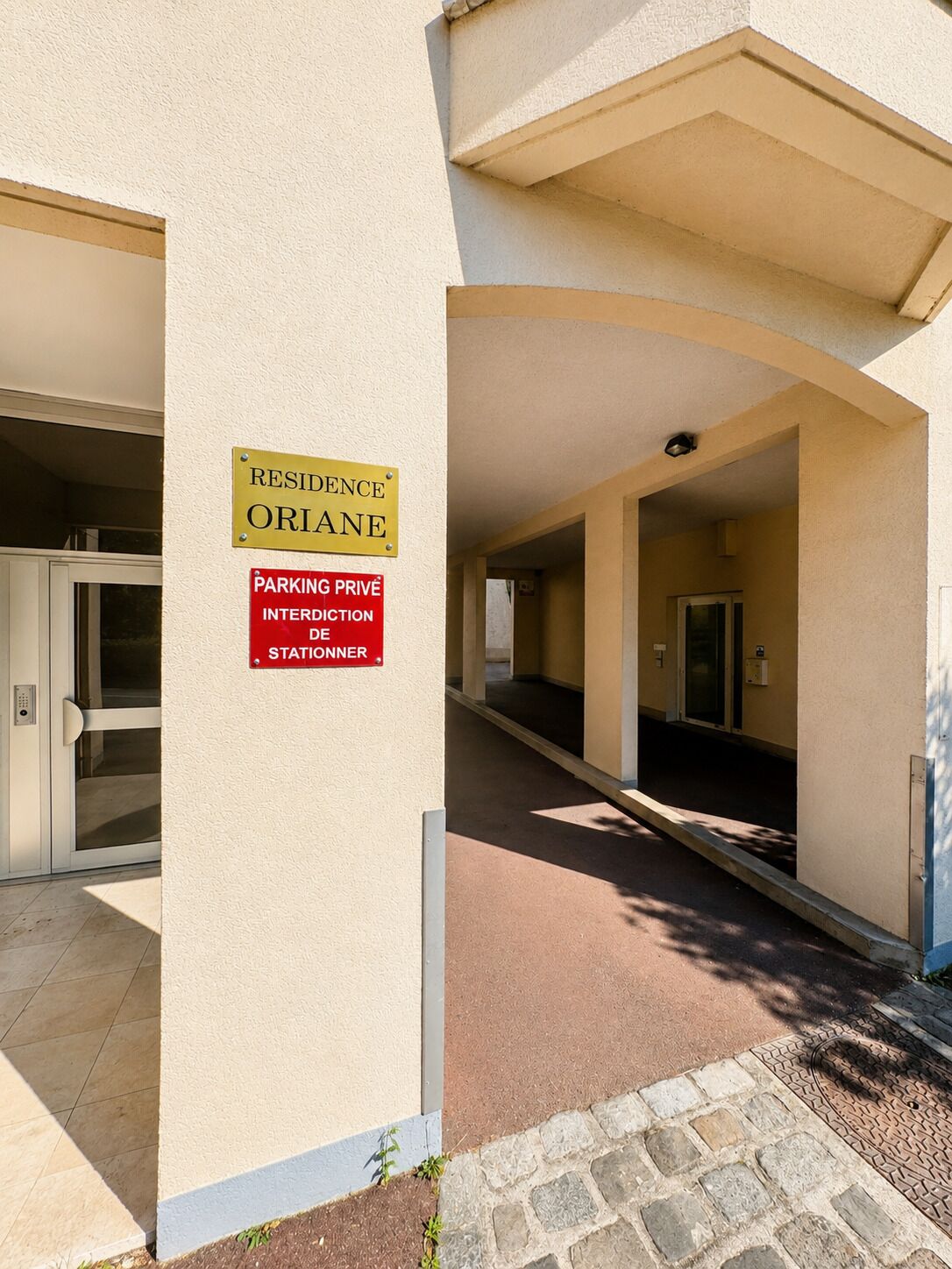 A building entrance with a sign indicating private parking and a residence named 'ORIANE.'