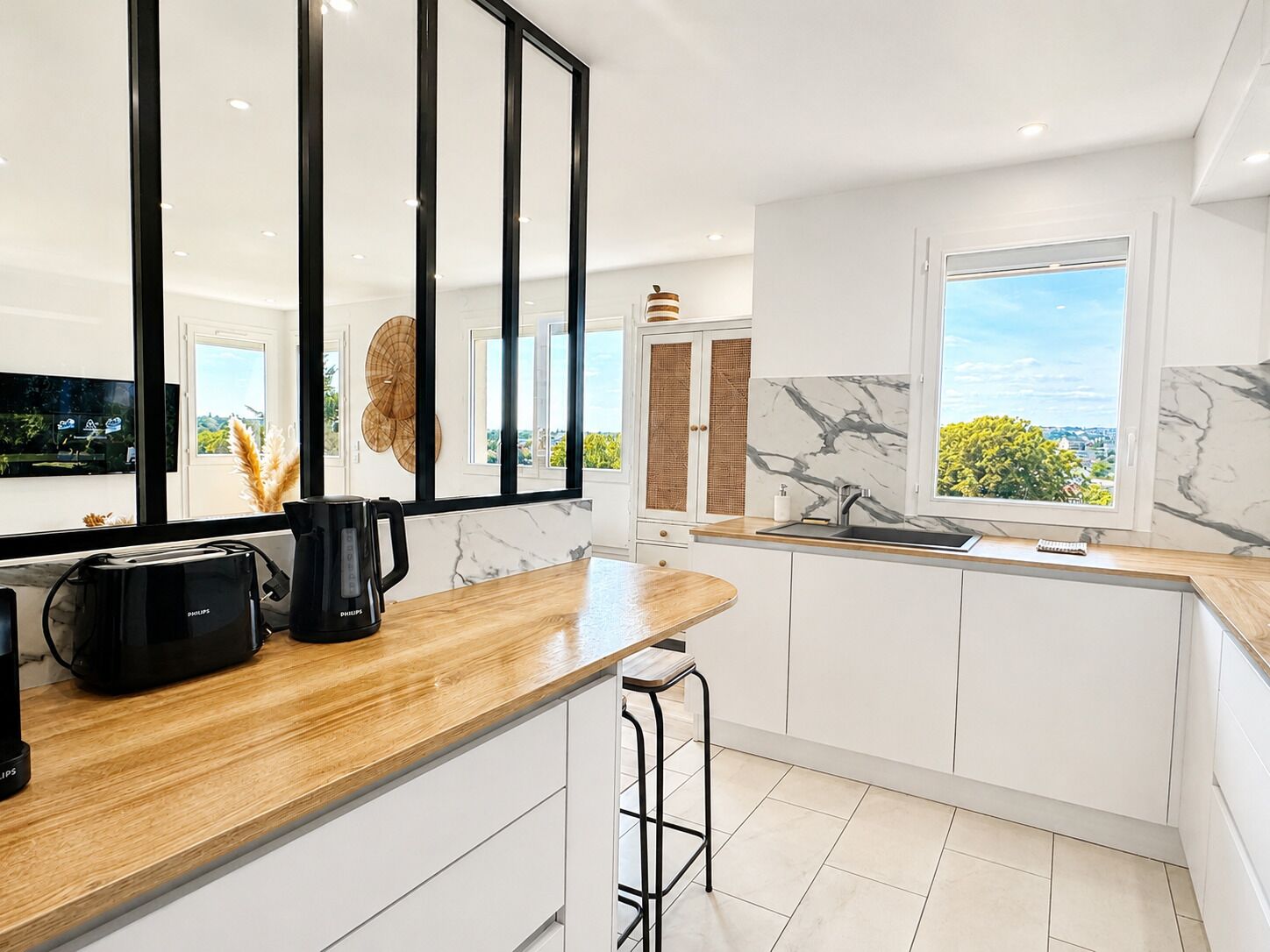 A modern kitchen with a wooden countertop, a black coffee maker, and a view of greenery outside.