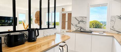A modern kitchen with a wooden countertop, a black coffee maker, and a view of greenery outside.