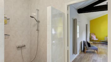 Un baño moderno con ducha, inodoro y lavabo. Se ve una puerta que da a una zona de estar con una pared amarilla y una silla.