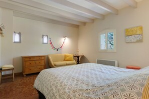 A bedroom with a bed, a wooden dresser, a chair, a window, and a wall-mounted lamp.