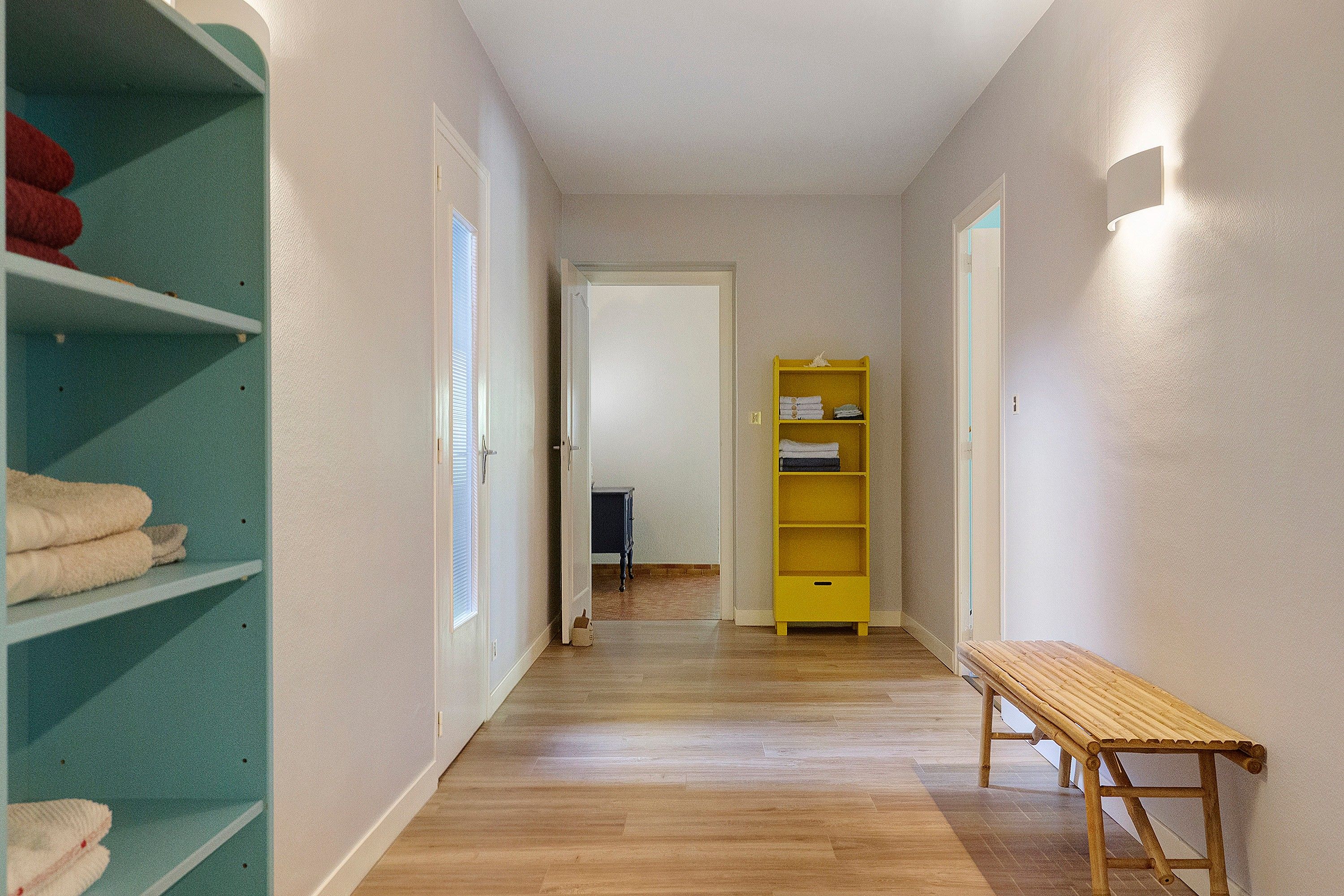 A hallway with a wooden bench, a green shelf with towels, and a yellow shelf with folded towels.
