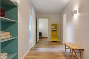 A hallway with a wooden bench, a green shelf with towels, and a yellow shelf with folded towels. - Villa Oléandre with Large Private Pool, Chassiers Ardèche (Chassiers)
