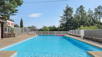 Una piscina rectangular con agua azul cristalina, rodeada por una solana de piedra y una valla blanca.
