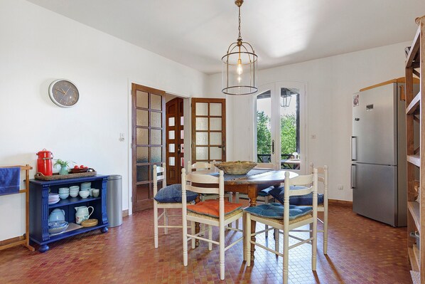 A kitchen with a dining table, chairs, a clock, and a refrigerator.