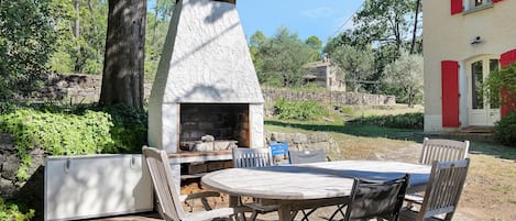 An outdoor patio with a stone-built wood-fired oven, a table, and chairs.