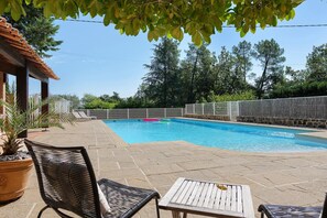 A swimming pool with a stone deck, surrounded by a white fence, and shaded by trees.