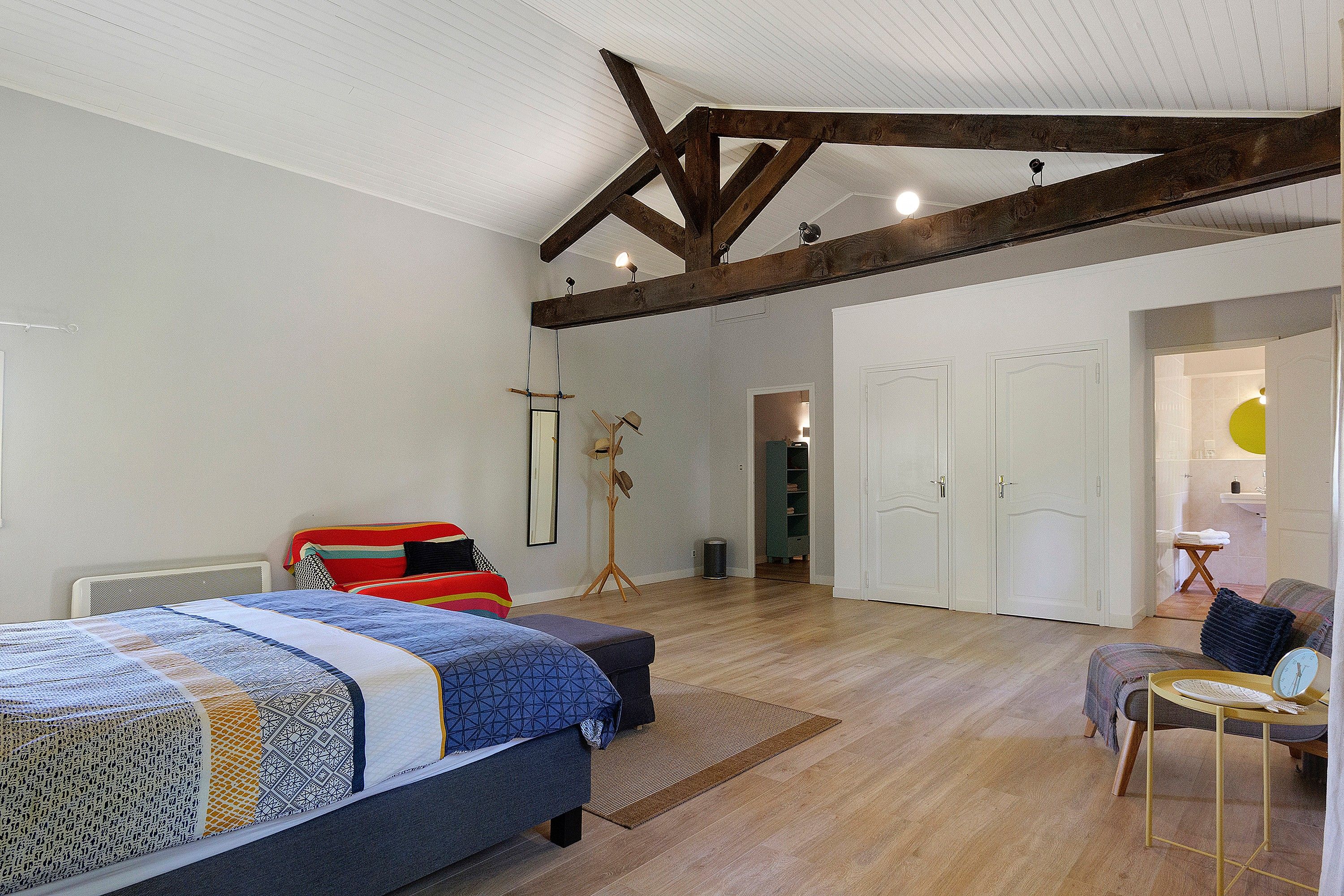 A bedroom with a large bed, a bedside table, a chair, a wardrobe, and a bathroom visible through an open door.