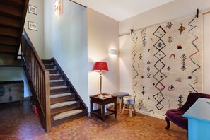 A staircase with a wooden handrail, a table with a lamp, a patterned rug, and a purple chair.