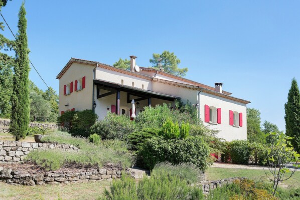 A two-story house with a stone wall in front, surrounded by greenery.
