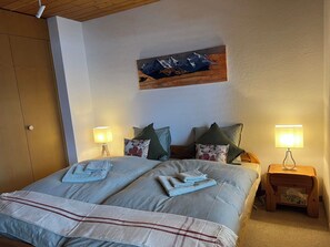 A double bed with a striped blanket, two bedside lamps, and a painting on the wall. - Möösli Vue by Interhome (Beatenberg)