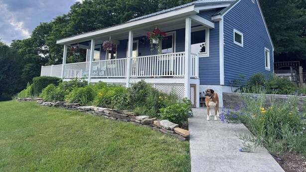 Ein zweistöckiges Haus mit Veranda, einem Hund auf den Treppen und einer Steinmauer im Vorgarten.