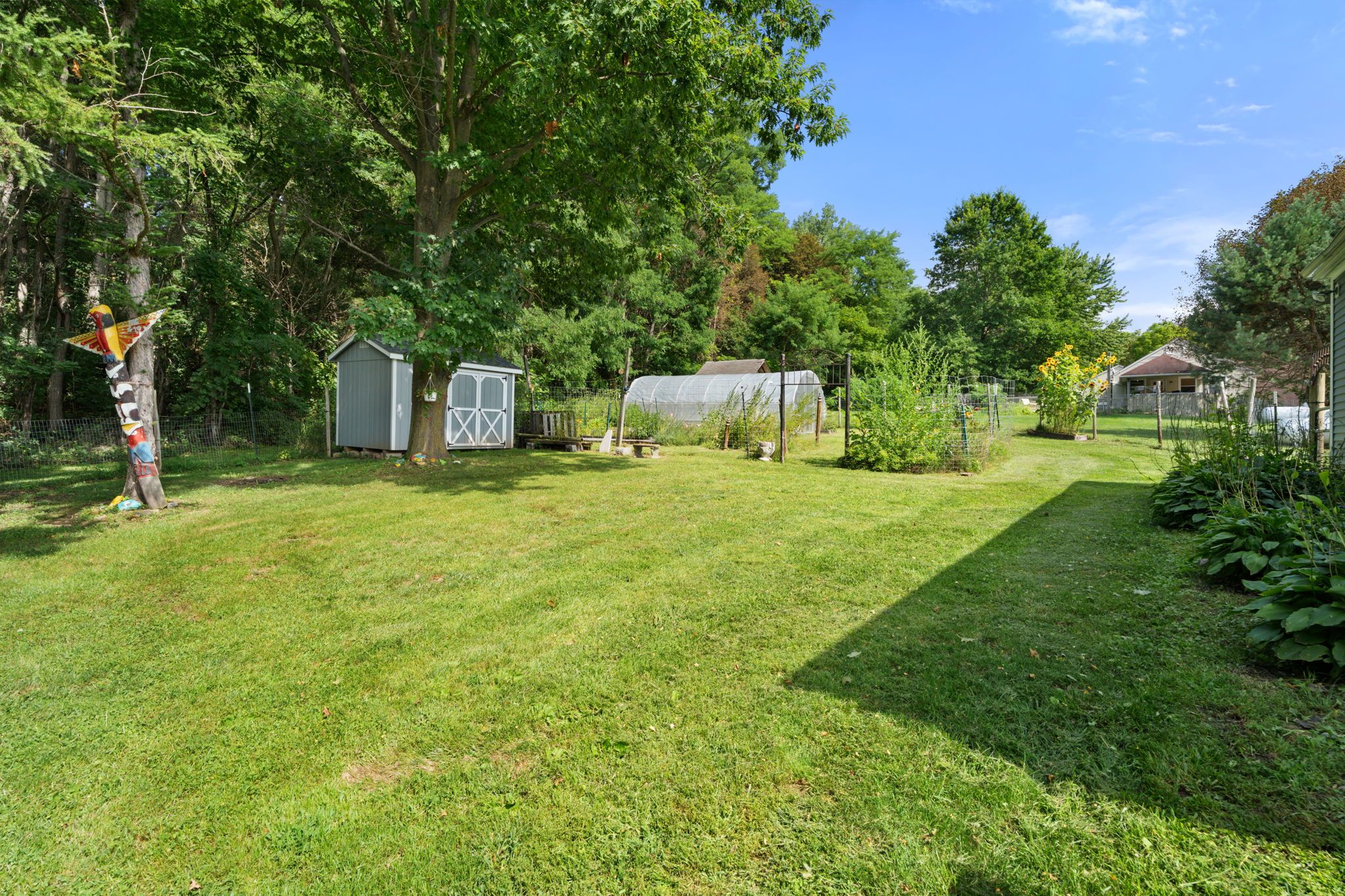 Un jardin bien entretenu avec une pelouse, un nichoir, une serre et une zone délimitée par une clôture.