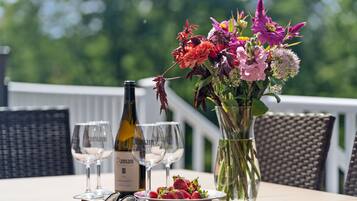 A table with a bottle of wine, two wine glasses, a vase with flowers, a bowl of strawberries, and a pair of sunglasses.