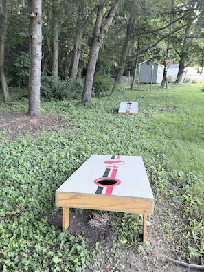 Un dardo de madera con diseño rojo y negro, sobre un área verde con árboles al fondo.
