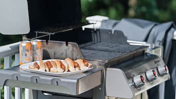 Un barbecue avec des saucisses et une assiette de saucisses, ainsi que deux canettes de bière.