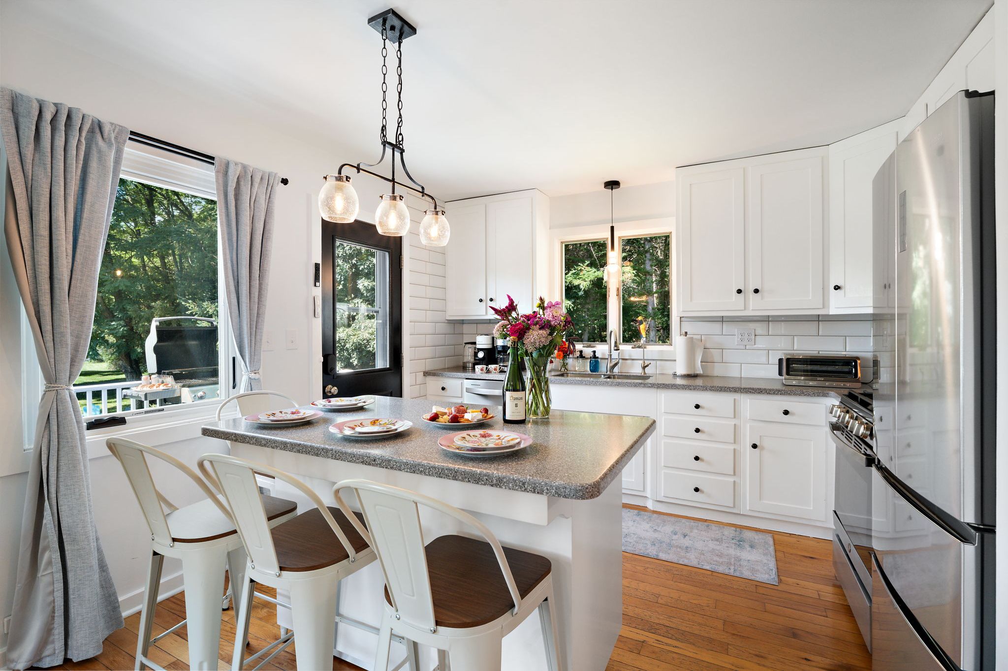 A modern kitchen with white cabinets, a stainless steel refrigerator, and a dining area with a table and chairs.